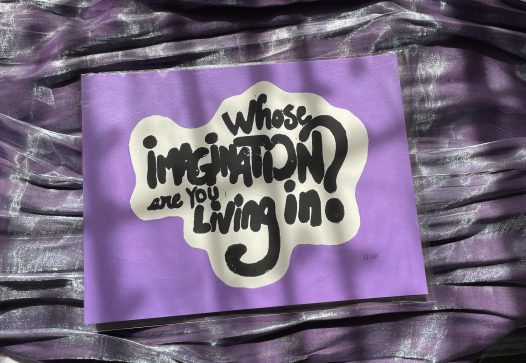 A print on watercolor paper with he words whose imagination are you living in? in black and the surrounding background is a soft purple. the print is on an iridescent purple fabric