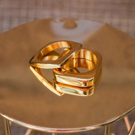  Two square gold out of the box rings on a gold table