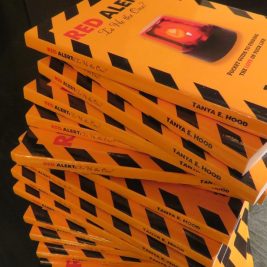 A stack of books with yellow covers and black stripes, featuring the title "RED ALERT" in large red letters, is prominently displayed. The cover design includes a red flashing light, suggesting a possible theme related to warnings or alerts in relationships.