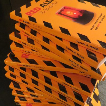 A stack of books with yellow covers and black stripes, featuring the title "RED ALERT" in large red letters, is prominently displayed. The cover design includes a red flashing light, suggesting a possible theme related to warnings or alerts in relationships.